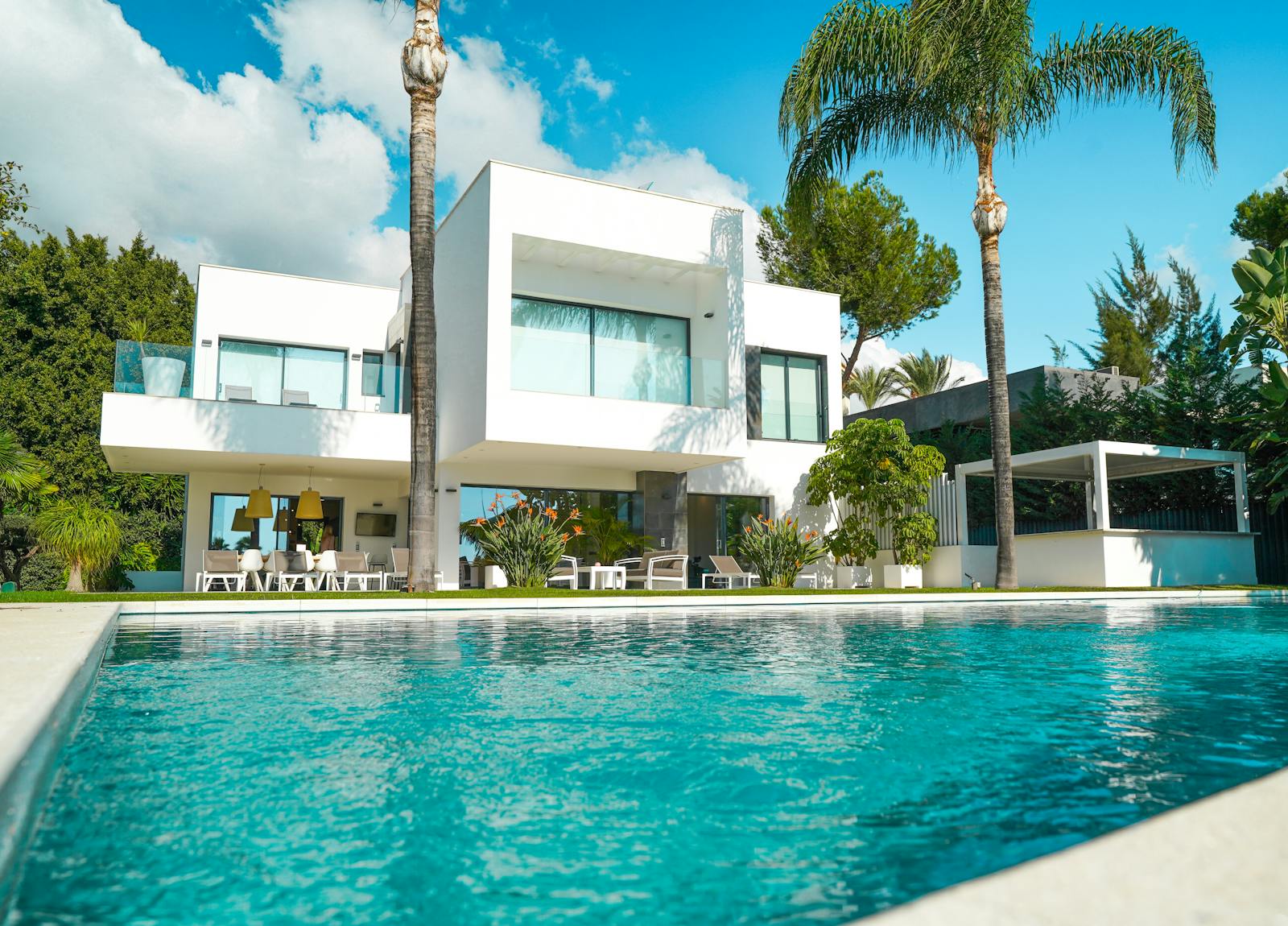 A modern white luxury villa with an infinity pool and palms